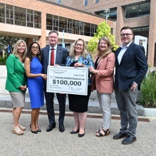 group of people standing outside, holding a giant check that says $100,000. 