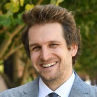man standing outside, arms crossed, smiling. 