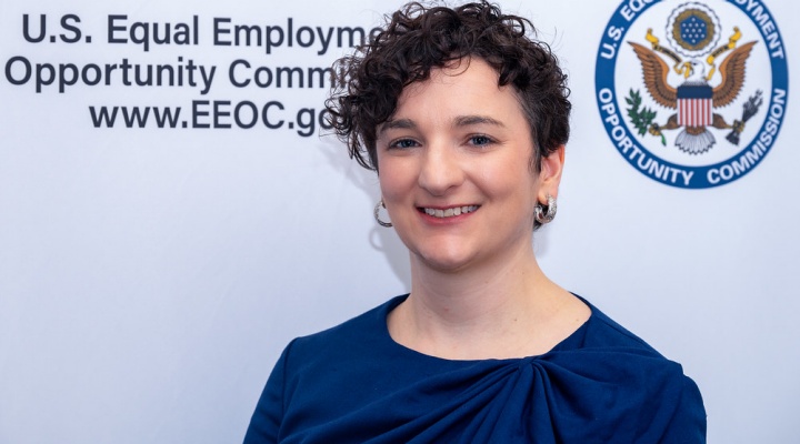 woman smiling, standing in front of a sign that says U.S. Equal Employment Opportunity Commission. 
