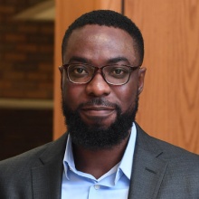 man standing with hands in his pocket, smiling. 