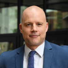 man standing outside glass windows, smiling. 