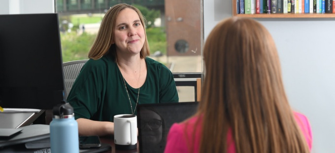 woman talking to a student across from her desk. 