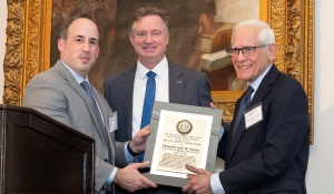 Three men staning, together holding up a plaque. 
