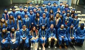 Large group of people sitting, wearing blue graduation regalia. 
