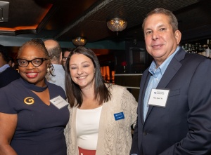 Three adults, smiling, attending a social event in a bar. 