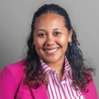 Studio portrait of a person wearing a bright magenta blazer over a pink and white striped shirt against a neutral background. 