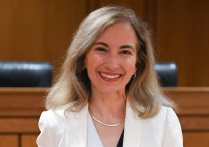Person wearing white blazer, standing in a courtroom. 