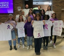 group photo of participants holding up handmade shirts about domestic violence awareness. 