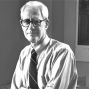 black and white photo of man sitting on a desk in his office. 