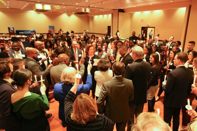 dinner attendees gathered, holding up lit candles in a wide circle formation. 