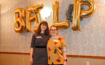 two women posed under balloons that spell BPILP. 