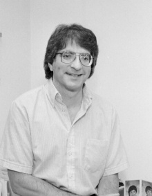 black and white photo of Atelson leaning against a desk inside a room. 