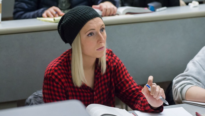 student wearing a knit cap taking class notes. 