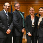 two men and two women wearing suits, smiling and standing in a courtroom. 