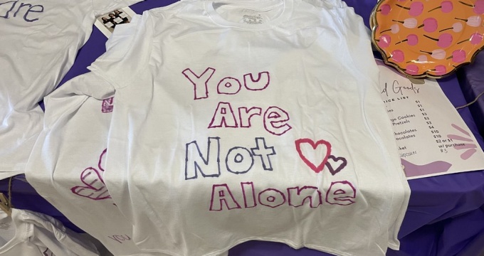 closeup photo of a white tshirt with the writing 'You are not alone' and a heart. 