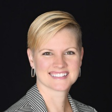 woman with short blond hair in front of a black background. 