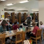 man talking to students sitting at a table in a library. 