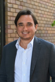 man smiling outside in front of a brick building. 