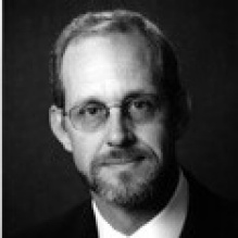 black and white photo of a man wearing a business suit, tie, and glasses. 