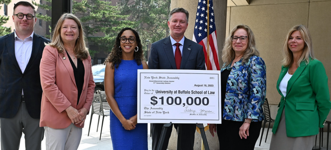 group of people standing smiling with a giant bank check that says $100,000. 