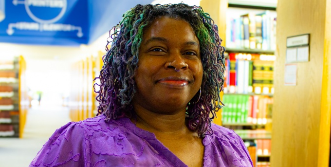 woman standing in a library, smiling. 