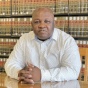 man sitting at table, behind him are shelves of law books. 