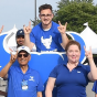 group of people gathered, wearing blue UB Bulls shirts, making the Bulls Horns gesture with their fingers. 