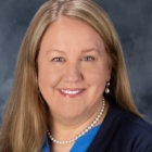 woman wearing pearls, blue shirt, smiling. 