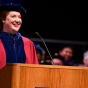 woman in red regalia standing at a podium, smiling. 