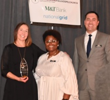 three people, smiling, one holding a glass award. 