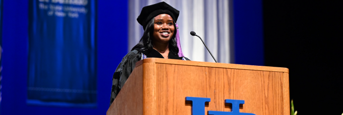 woman wearing commencement regalia speaking at a podium. 