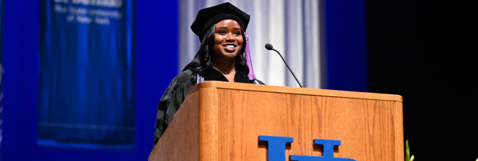 woman wearing commencement regalia speaking at a podium.