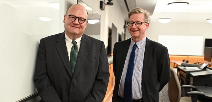 two men standing in a classroom, smiling. 