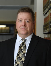 man smiling, standing in front of bookshelves. 