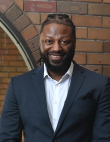 smiling man standing in front of a brick wall. 