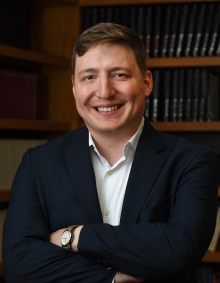 smiling man in front of bookshelves. 