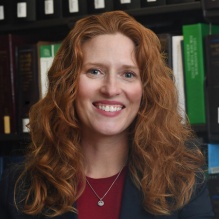 woman smiling standing in front of a library bookshelf. 