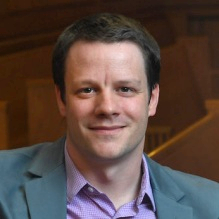 man smiling, sitting on a courtroom bench. 