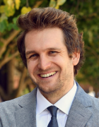 man wearing a suit inside a hallway, smiling. 