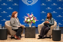 two women sitting in chairs on a stage, behind them large blue screen that says UB - University at Buffalo. 