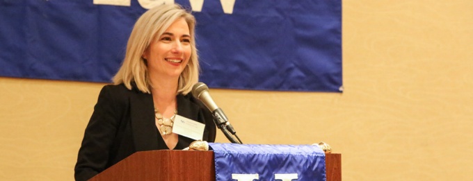 woman standing at a podium, speaking for an event. 