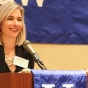 woman standing at a podium, speaking for an event. 