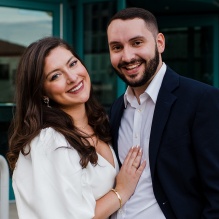 woman and man, smiling, standing outside a building. 