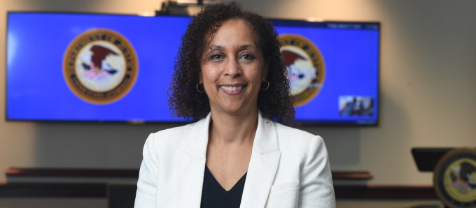 woman inside a media room, wearing white blazer, smiling. 