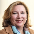 woman wearing beige blazer, blue scarf, smiling. 