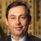 man standing in front of window of high-rise building, smiling. 
