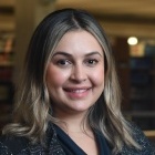 woman standing in front of bookcase, smiling. 