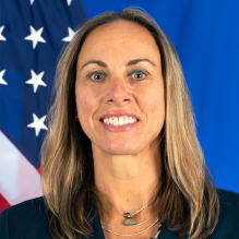 woman smiling, standing in front of a US flag. 