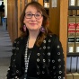 woman in a library standing next to a bookcase. 