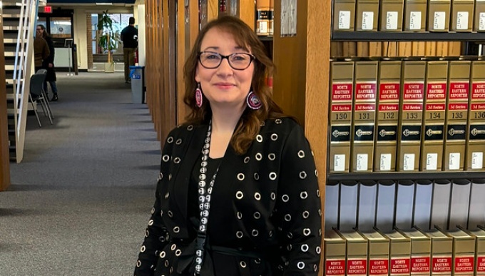 woman staning in a library in front of several bookcases. 